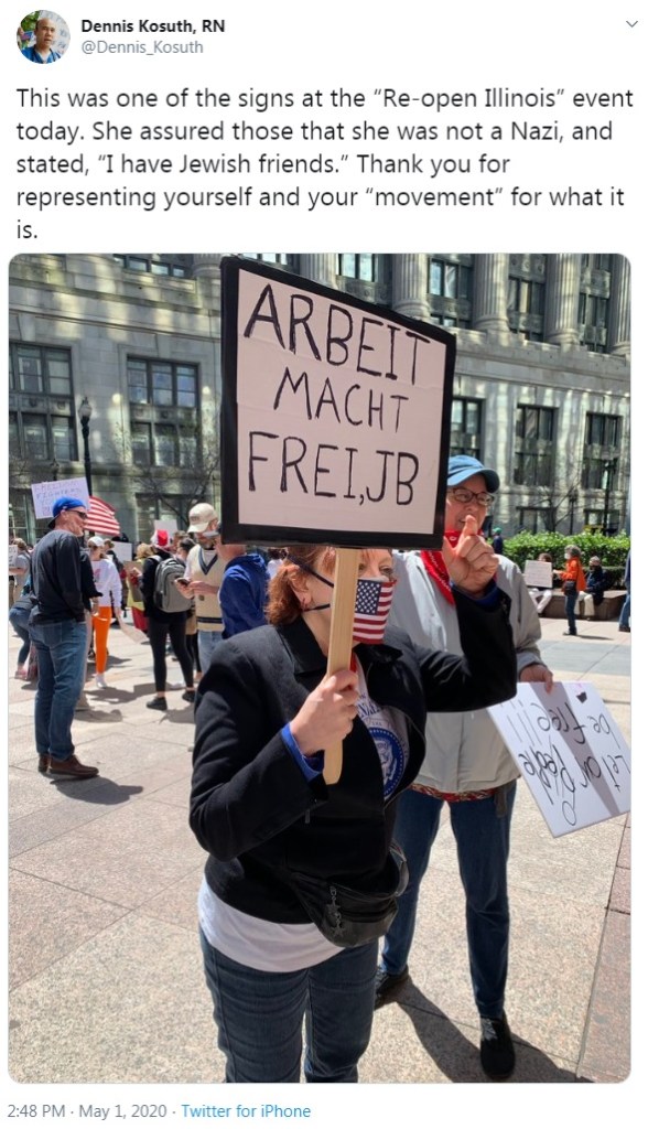 anti-lockdown protester holds a sign reading ARBEIT MACHT FREI
