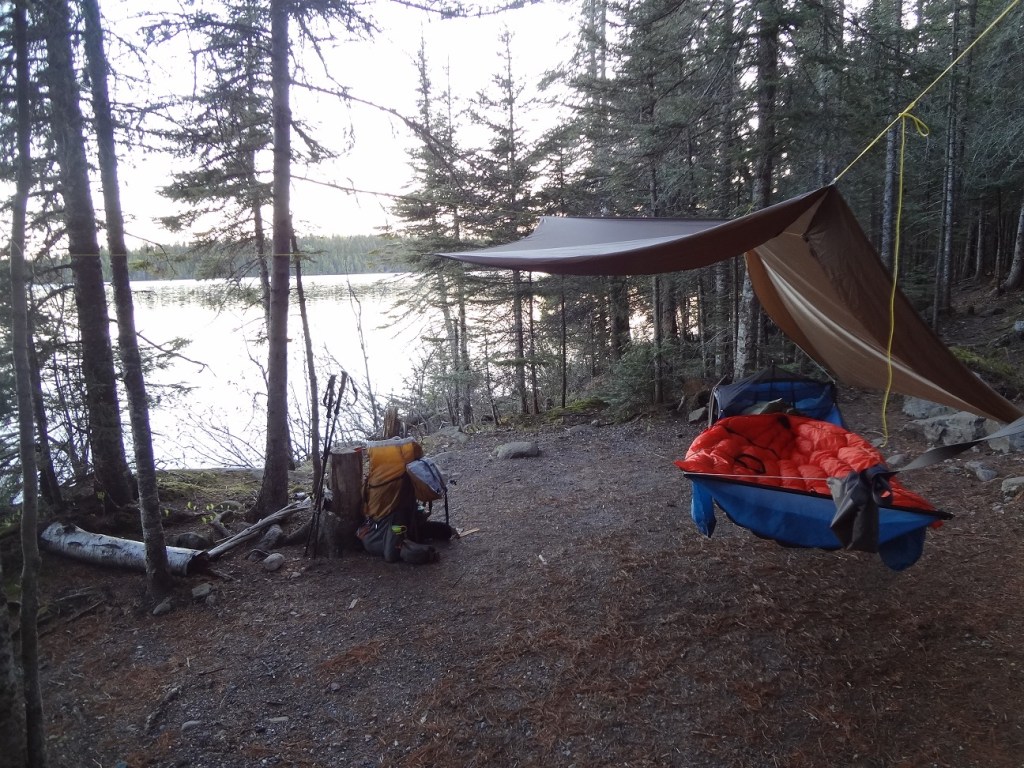 photo of campsite # 5 at Lane Cove, Isle Royale National Park - a hammock is slung between two trees to the right, various backpacking gear sits on the ground to the left, a view of Lane Cove is in the background through the trees