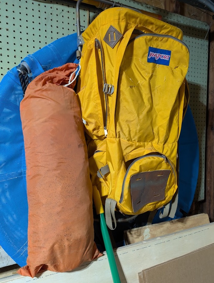 a Eureka Timberline tent in its stuff sack standing alongside a yellow JanSport rigid-frame backpack; both are 50 years old