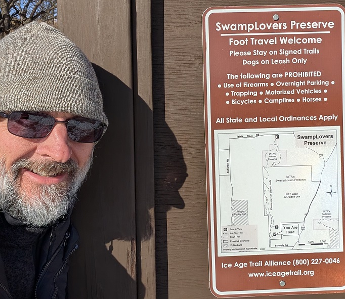 the author in a gray knit cap and dark glasses, posing next to a map of the trail