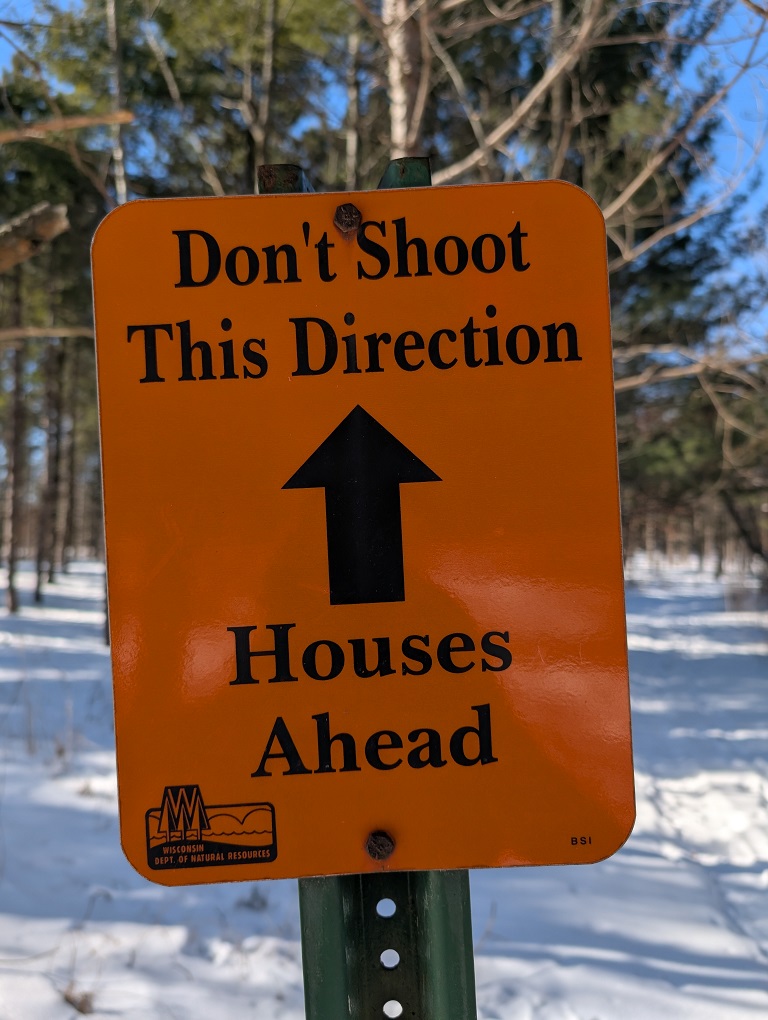 orange sign with the words "Don't shoot this direction, houses ahead"