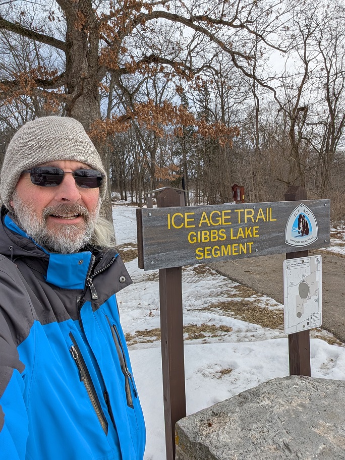 a bearded man poses beside a trailhead sign for the Gibb's Lake segment of the Ice Age Trail