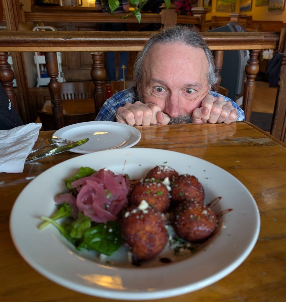 an old man hunches over a plate of potato croquettes placed in the middle of a table in a local restaurant