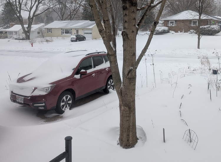 drifted snow covers the front yard and driveway of a suburban home